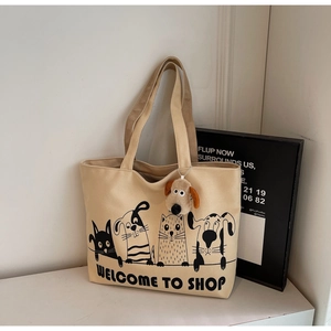 Close-up of beige canvas tote bag with cartoon pets and plush dog head charm detail