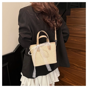 Detail of hand-woven straw bag featuring a large white lace bow and leather handles