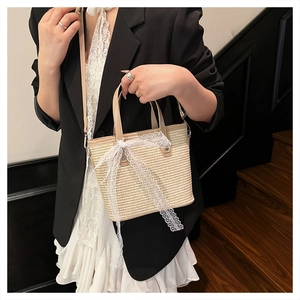 Elegant woven straw crossbody bag with large white lace bow detail shown on a model