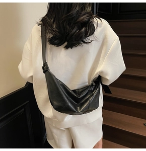 Detail of black leather croissant bag showing vertical stitching and knotted strap design