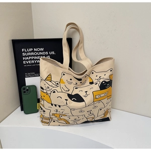 Detailed view of beige canvas tote bag featuring a cute cartoon cat illustration
