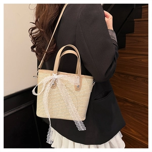 Detailed view of woven straw handbag with brown leather trim and white lace ribbon