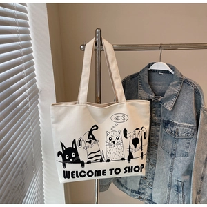 Detail of beige canvas tote bag featuring whimsical cartoon cat and dog illustrations