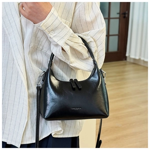 Close-up of a glossy black crescent moon bag featuring metallic dual zippers and leather texture