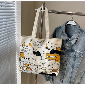 Detail of off-white canvas tote bag featuring playful cartoon cat prints and sturdy straps