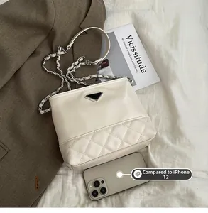 Size comparison of beige quilted bucket bag with silver chain against an iPhone 12