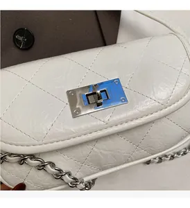 Detail of silver rectangular twist lock and quilted leather texture on white chain bag