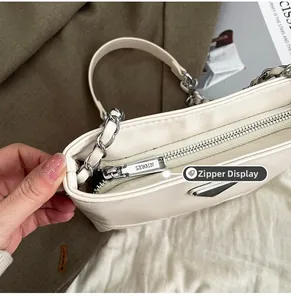 Detailed close-up of silver zipper with engraved lettering and chain handle on white bag