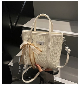 Close-up of white woven leather bucket bag with lace bow charm and metal nameplate