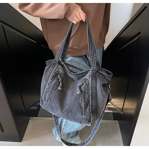 Close-up of washed denim tote bag showing distressed texture and double zipper details