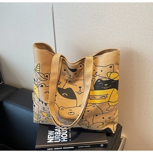 Detail of khaki canvas tote bag with cartoon cat prints on a leather surface