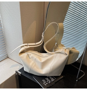 Detailed view of cream hobo bag with pleated leather texture on a dark cabinet