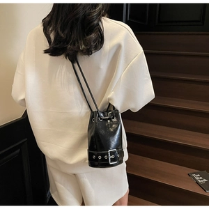 Détail du sac seau noir brillant avec boucle argentée porté en bandoulière par un modèle