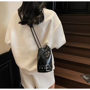 Détail du sac seau noir à cordon avec finition brillante et boucle métallique sur un modèle