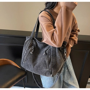 Detail of washed grey denim tote bag featuring dual vertical zippers and removable strap