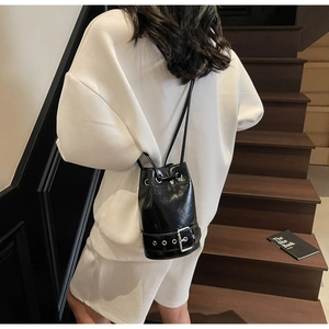 Détail du sac seau noir brillant avec boucle argentée et accents d'œillets métalliques