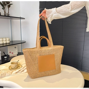 Detail of hand-woven straw tote bag featuring brown leather patch and dual shoulder straps