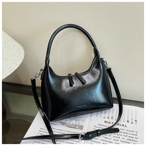 Detailed view of black crescent underarm bag with double zippers on a glass table