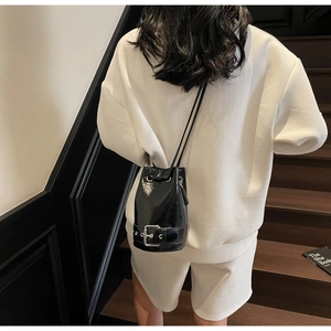 Détail du sac seau en cuir verni noir avec grande boucle argentée et cordon de serrage