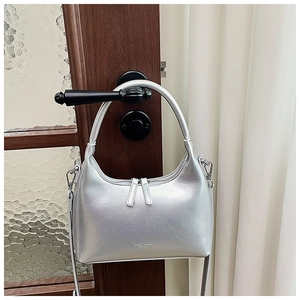 Silver metallic crescent bag with dual zippers hanging on a dark wood door handle