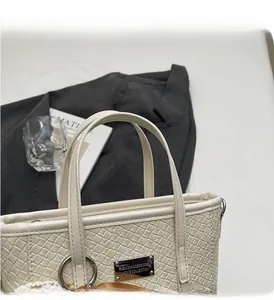 Dettaglio della borsa a secchiello intrecciata crema con placca logo in metallo argento