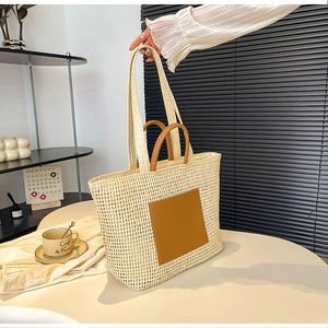 Detail of hand-woven beige straw tote bag featuring brown leather handles and square patch