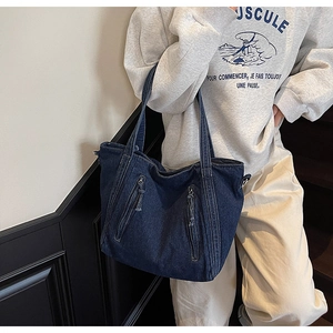 Detail of a large dark blue denim tote bag with dual vertical zipper pockets on steps