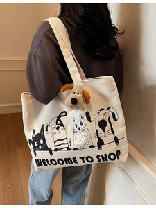 Off-white canvas tote bag with cartoon pet prints and plush dog charm on shoulder
