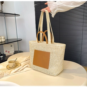 Detail of a beige woven straw tote bag with brown leather patch on a stylish white table