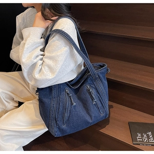 Detail of blue denim tote bag with decorative diagonal zippers on wooden steps