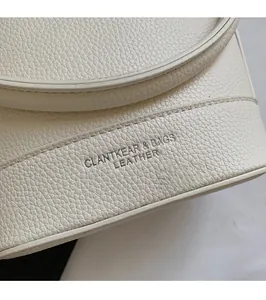 Gros plan sur la texture cuir litchi blanc crème et le logo embossé du sac à main chic