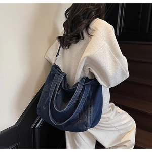 Detail of dark blue denim tote bag featuring dual straps and white contrast stitching