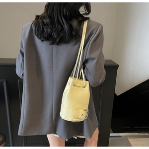 Vue de dos d'un sac seau jaune avec cordon et boucle sur un blazer gris foncé