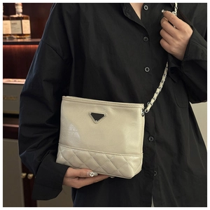 Detailed view of beige quilted bucket bag with chain strap worn by a model