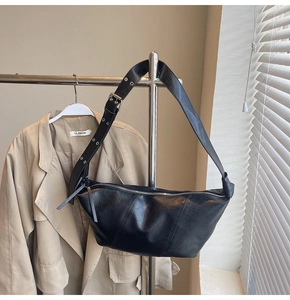 Detail of black faux leather half-moon bag featuring wide strap with silver eyelets