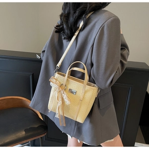 Detail of cream bucket bag with crocodile texture and decorative lace bow on a blazer