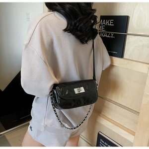 Close-up of black quilted patent leather mini chain bag worn on a grey stylish outfit