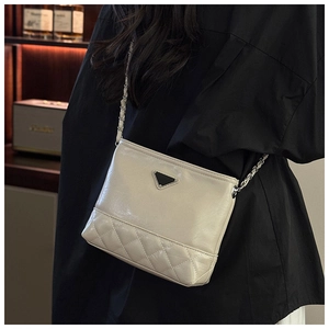 Detail of cream-colored quilted shoulder bag with chain strap and triangular metal plaque