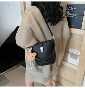 Détail d'un sac seau en cuir noir grainé avec un pendentif ours en peluche beige mignon