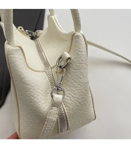 Detalle del bolso tipo cubo de cuero blanco granulado con cremallera y herrajes plateados