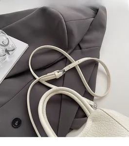 Detalle de bolso de mano en cuero blanco con textura de lichi y correa ajustable fina