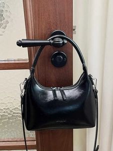 Minimalist black glossy leather crescent hobo bag hanging on a dark brown wooden door