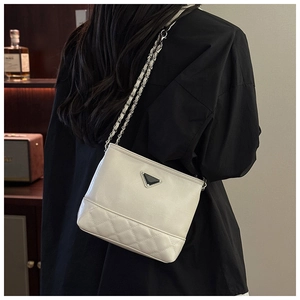 Detail of cream chain bucket bag showing glossy leather, metal plaque, and quilted pattern