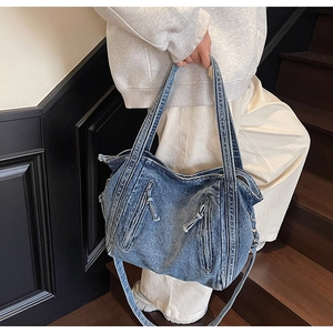 Detail of blue denim tote bag with zippers and straps on a wooden staircase model