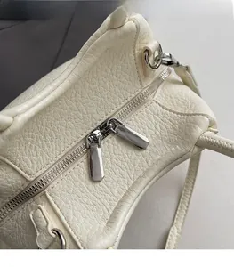 Detalle de cremallera doble plateada en bolso de piel granulada blanco crema