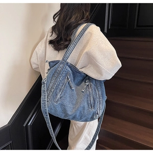 Detail of blue denim tote bag featuring dual vertical zippers and rugged wash texture