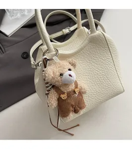 Detalle del bolso tipo cubo en cuero granulado blanco crema con un tierno colgante de oso