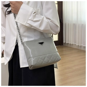 Detailed view of grey quilted leather handbag with silver chain strap and metal emblem
