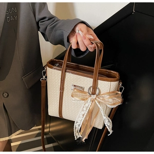 Dettaglio borsa a secchiello intrecciata crema con bordo marrone e fiocco decorativo