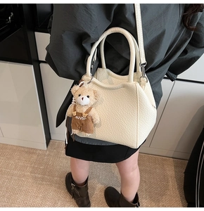 Detalle del bolso tote de cuero crema con grabado de lichi y colgante de oso de peluche